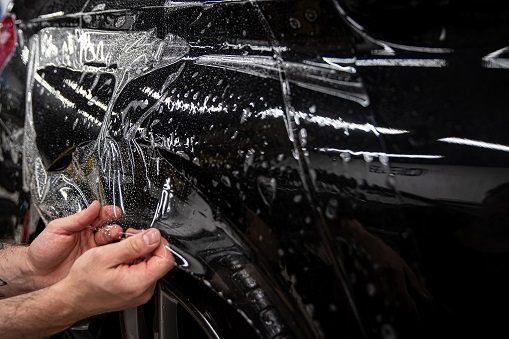 car detailing studio worker Appling transparent paint protection film on car body.